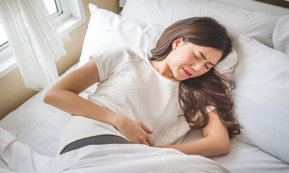 woman lying in bed holding stomach with abdominal cramps before periods and menstrual pain