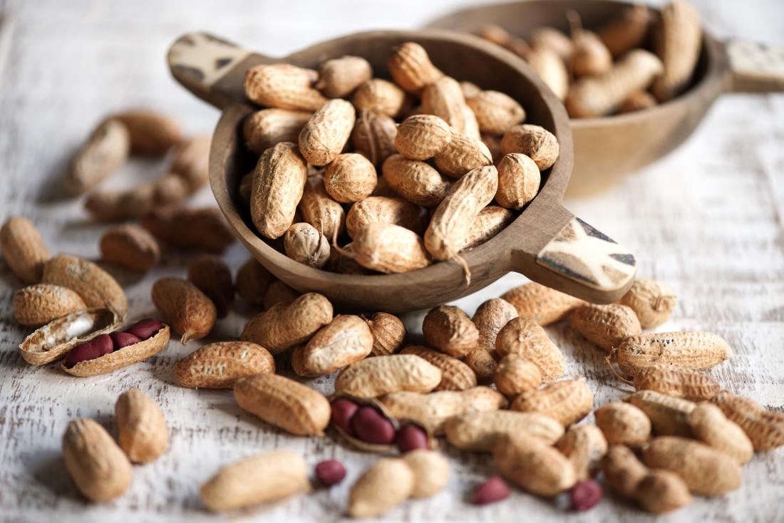 peanuts in and out of shells spilling out of wooden bowl