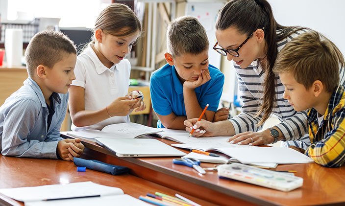 elementary school teacher helping students with lesson 704x421 1