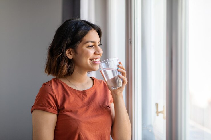 smiling young arab female drinking water while standing near window home 116547 50145 1